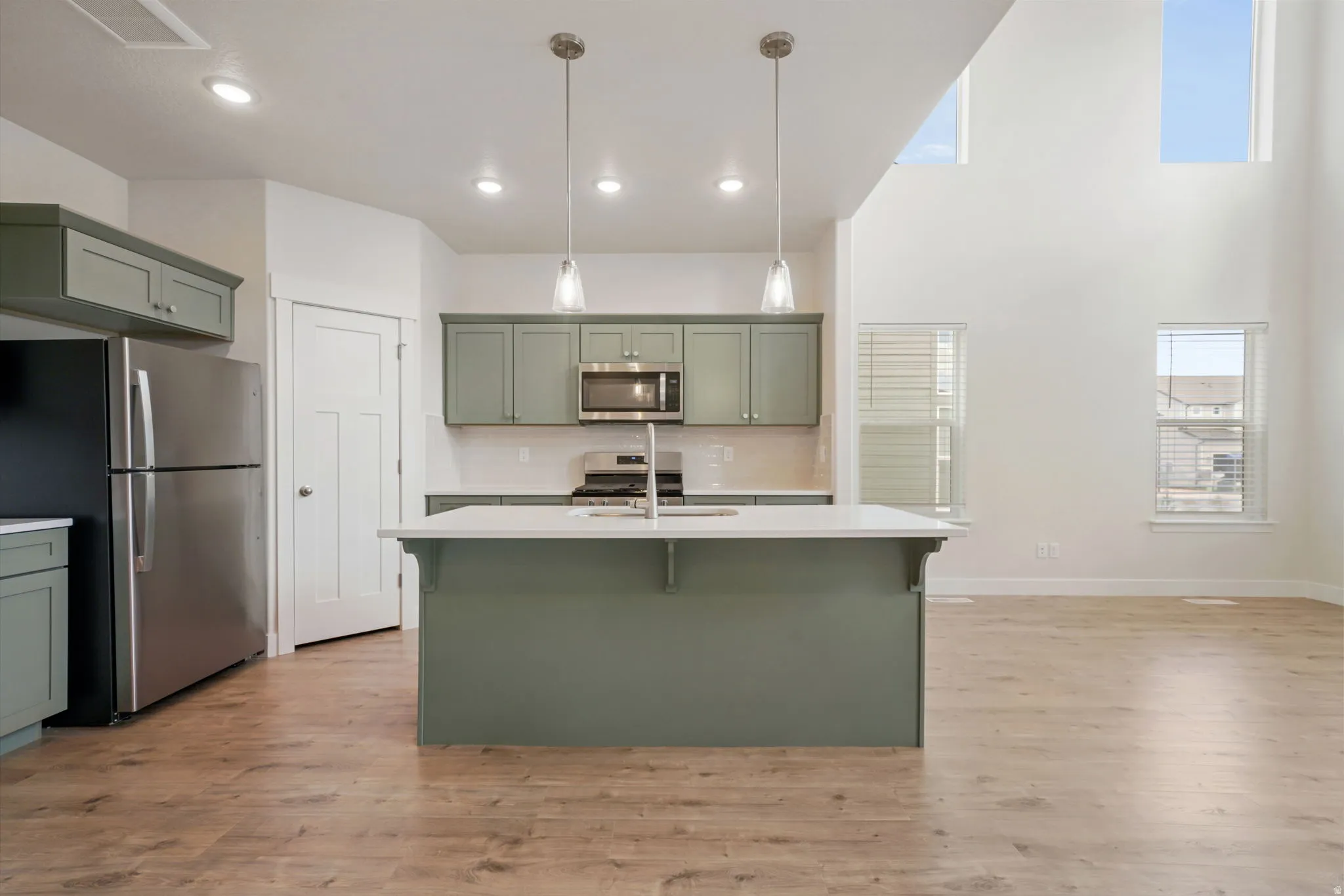 Open-concept kitchen featuring a central island with integrated sink, coordinating cabinetry, stainless steel appliances, and wood-finish flooring