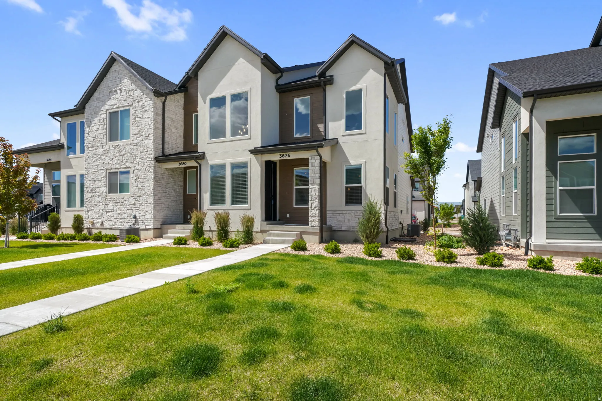 Modern townhome exterior featuring a stucco and stone facade, dark trim accents, multiple large windows, and a paved walkway leading to the entrance