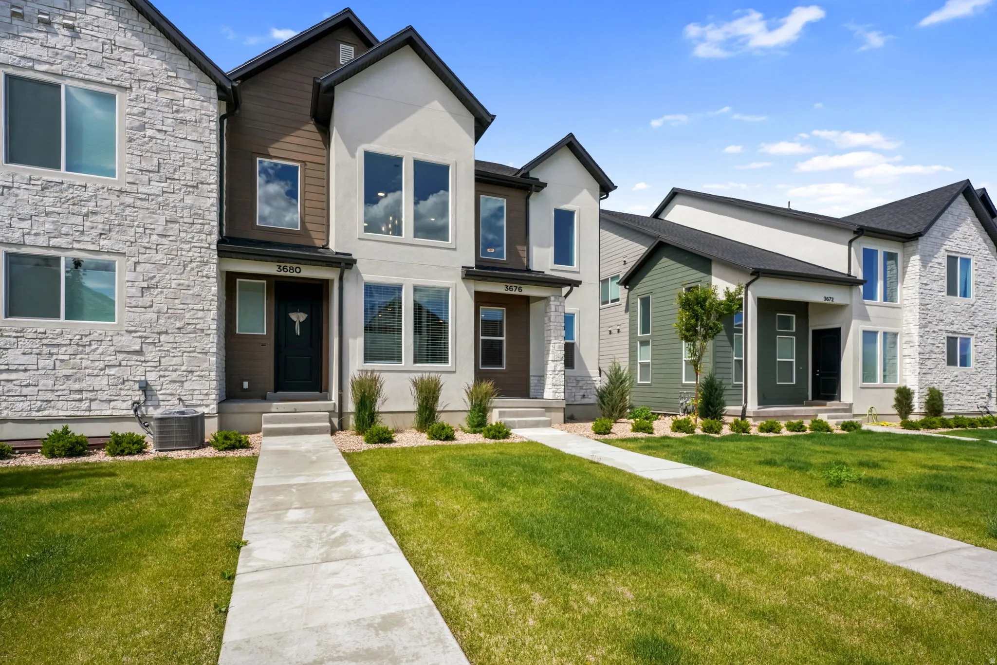 Contemporary townhome exterior featuring a combination of light stucco, dark wood-finish siding, and white stone veneer