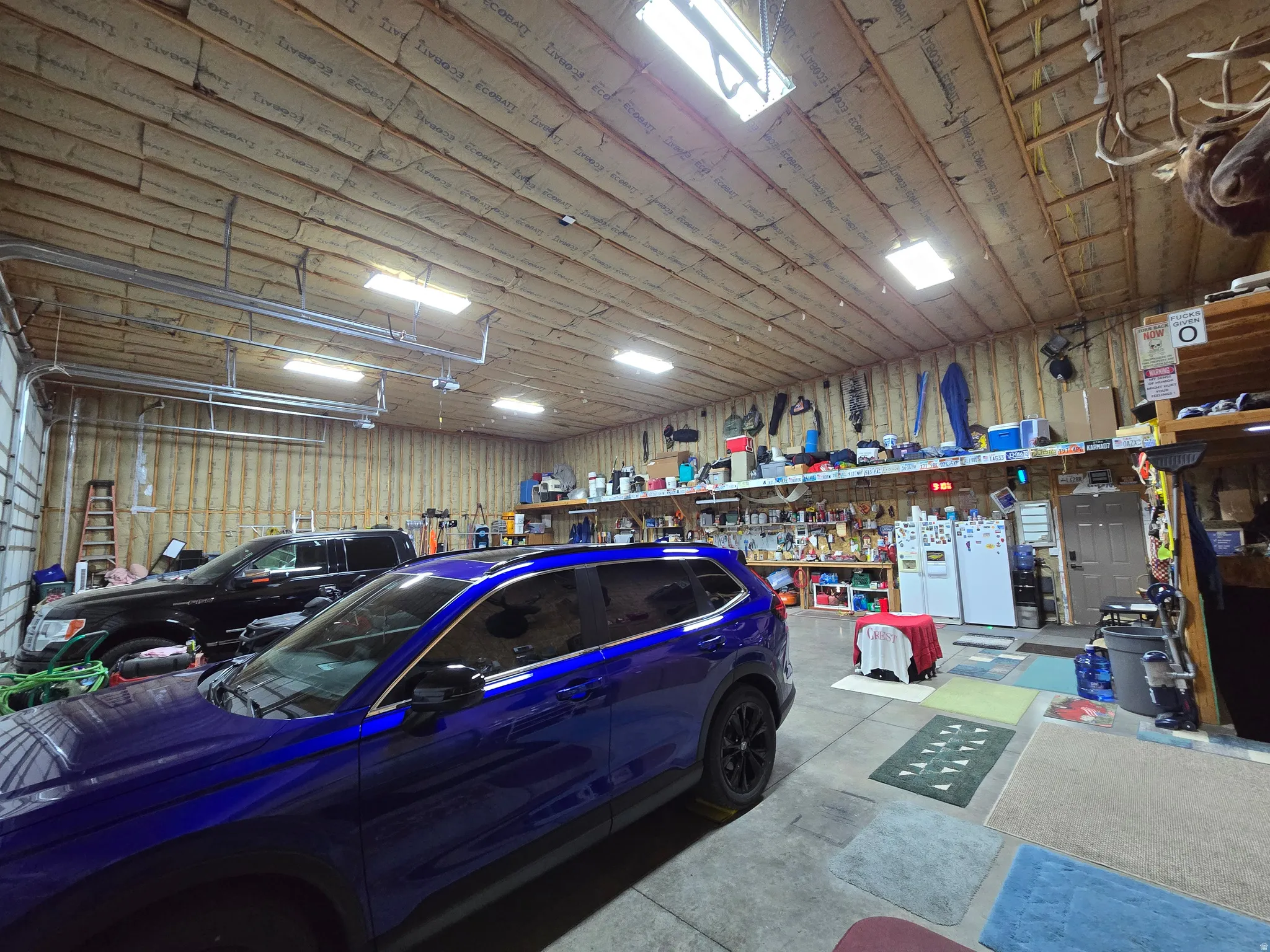 Spacious garage featuring a high, exposed ceiling with insulation, ample overhead lighting, and concrete flooring