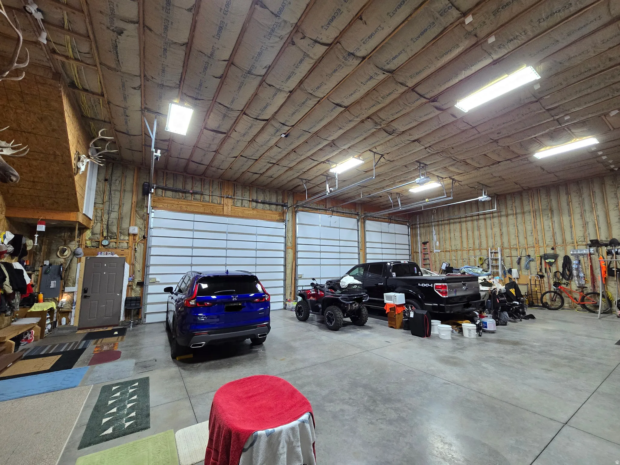 Spacious garage featuring a concrete floor, two large overhead doors, exposed wood framing, and fluorescent lighting