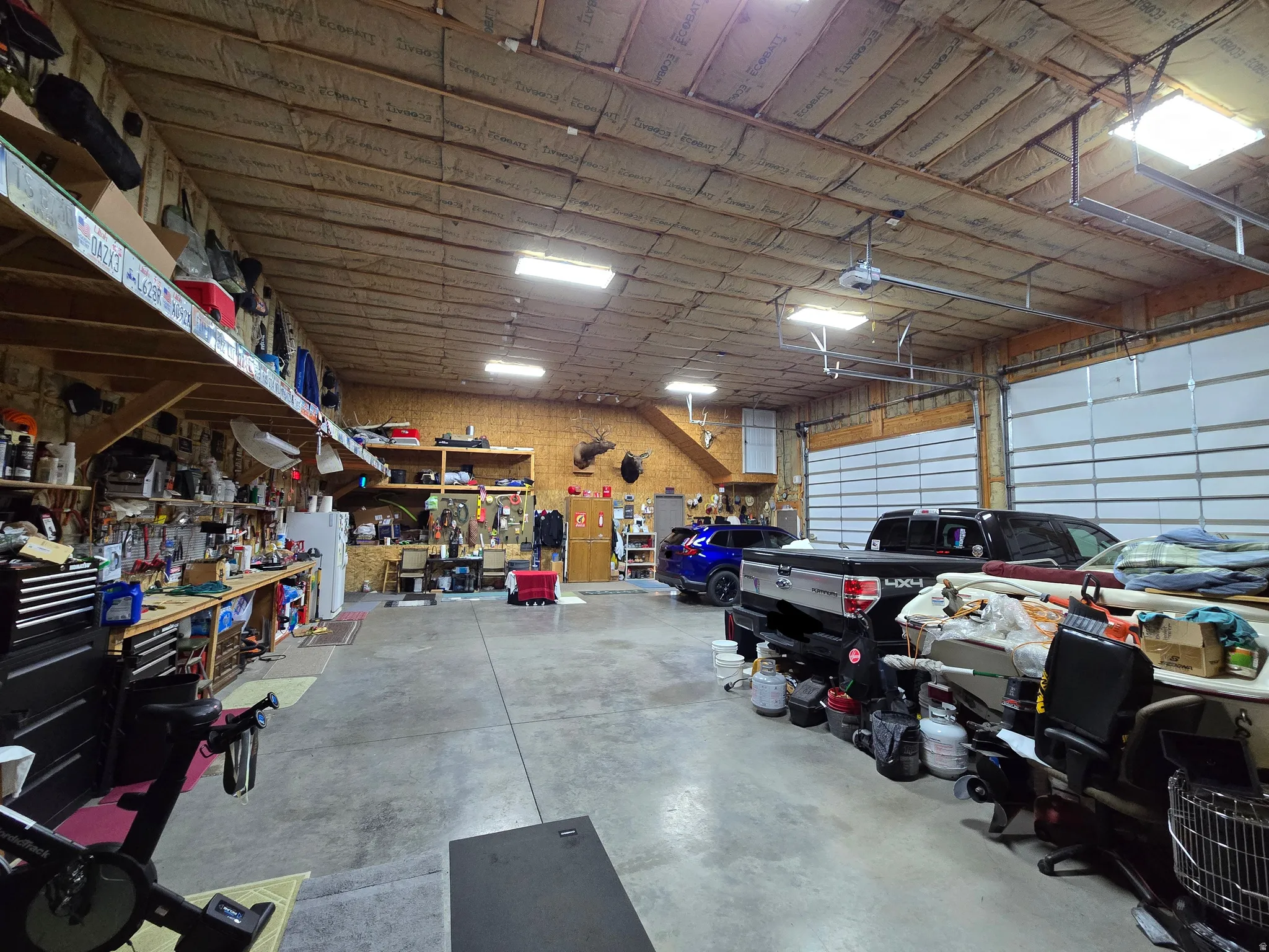 Spacious garage with high ceilings, multiple overhead garage doors, exposed wood beam construction, concrete flooring, and built-in shelving