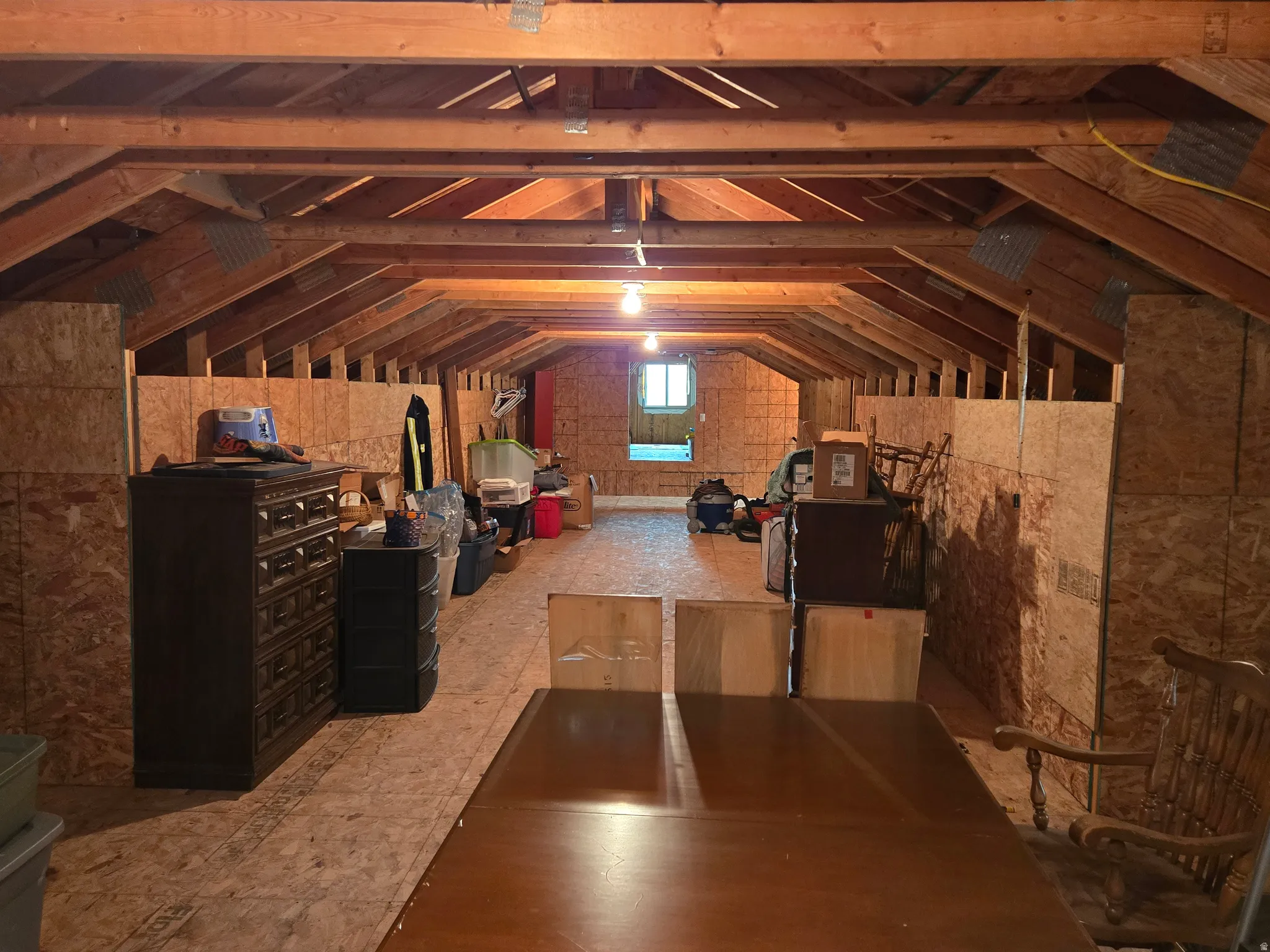 Expansive attic space featuring exposed wood rafter beams, plywood flooring, and a rear window