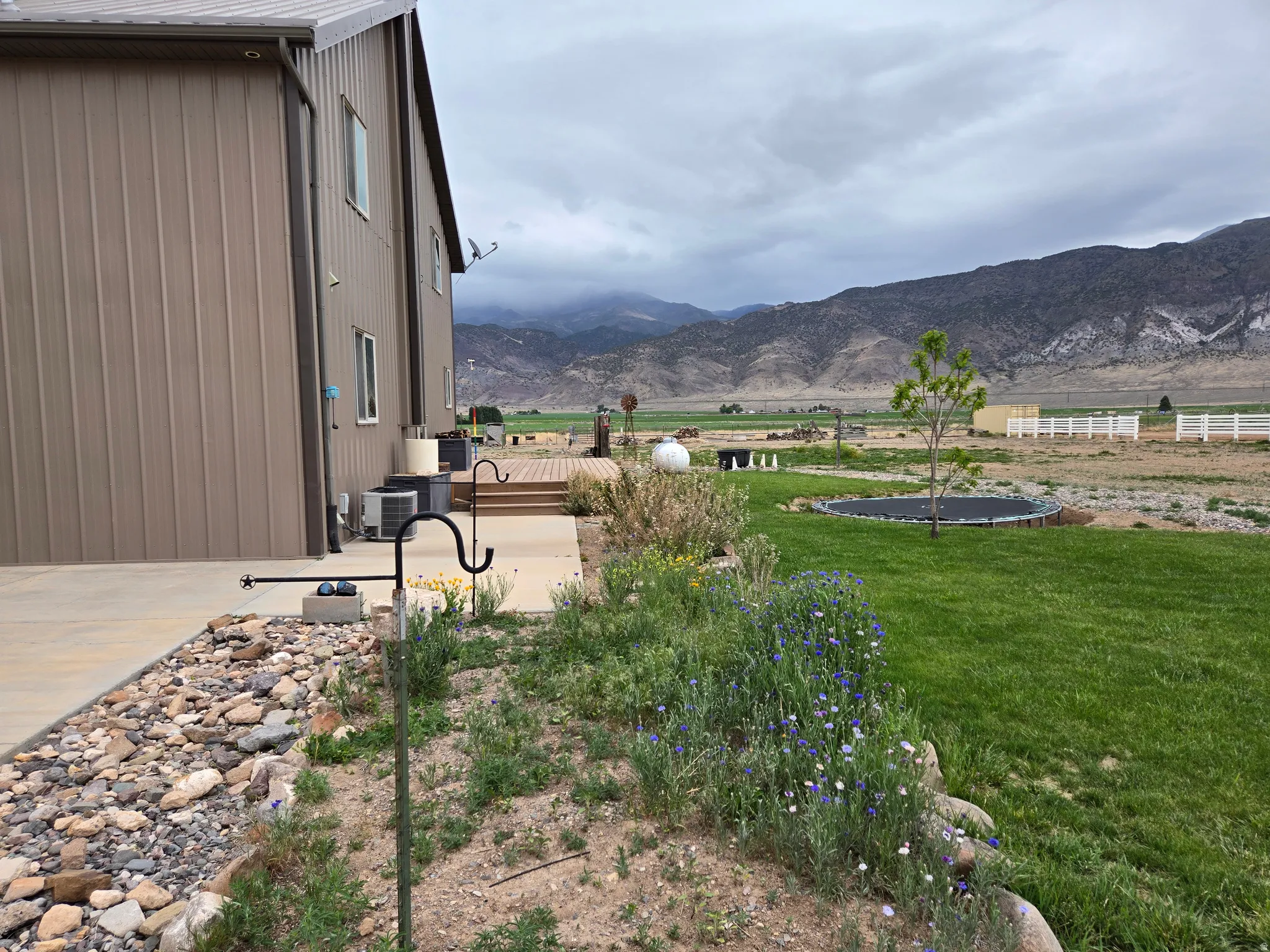 Expansive exterior featuring a brown metal-sided structure, concrete patio, wooden deck, and a lush lawn