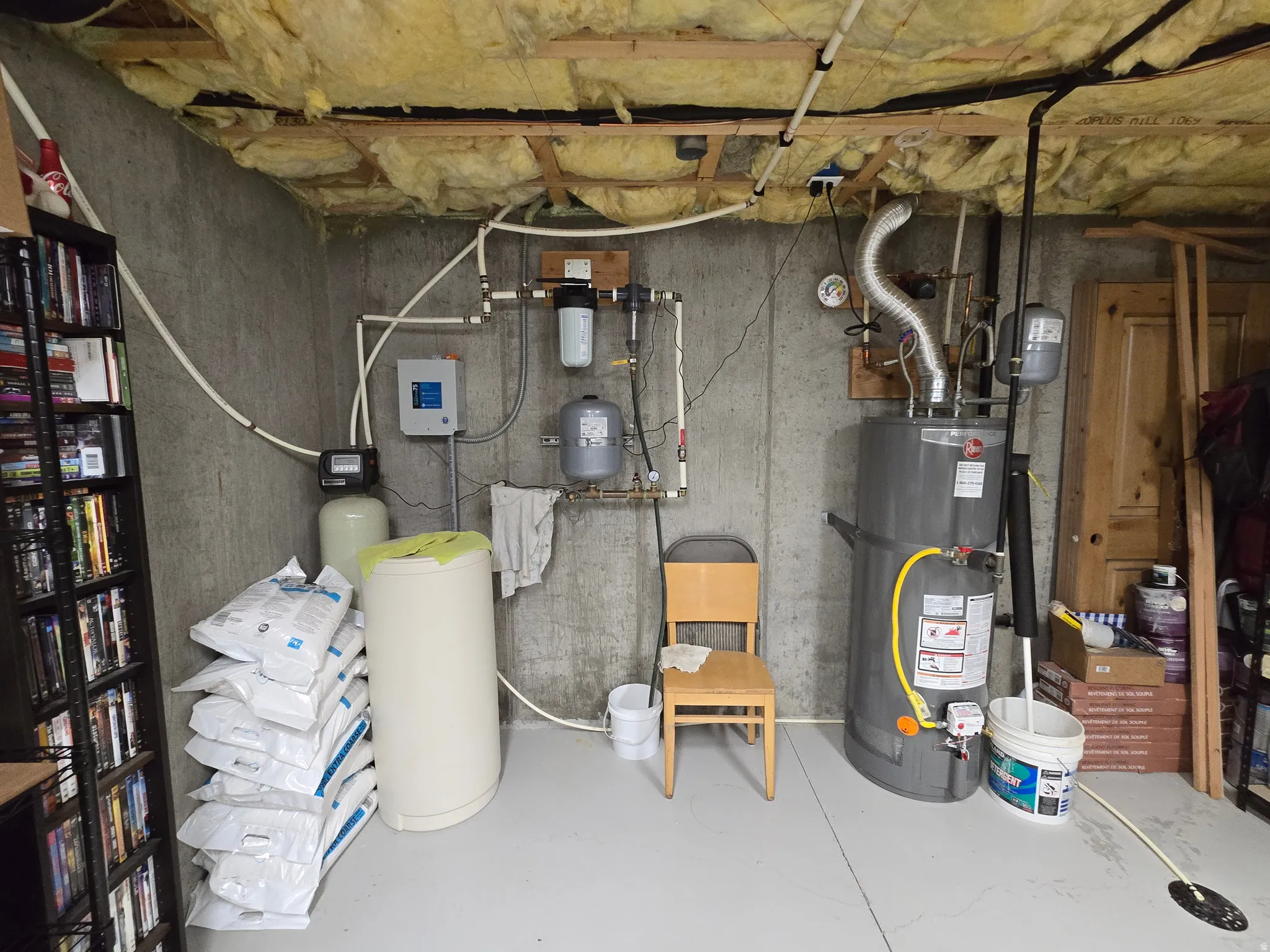 Utility room featuring a water heater, water filtration system, and exposed ceiling insulation
