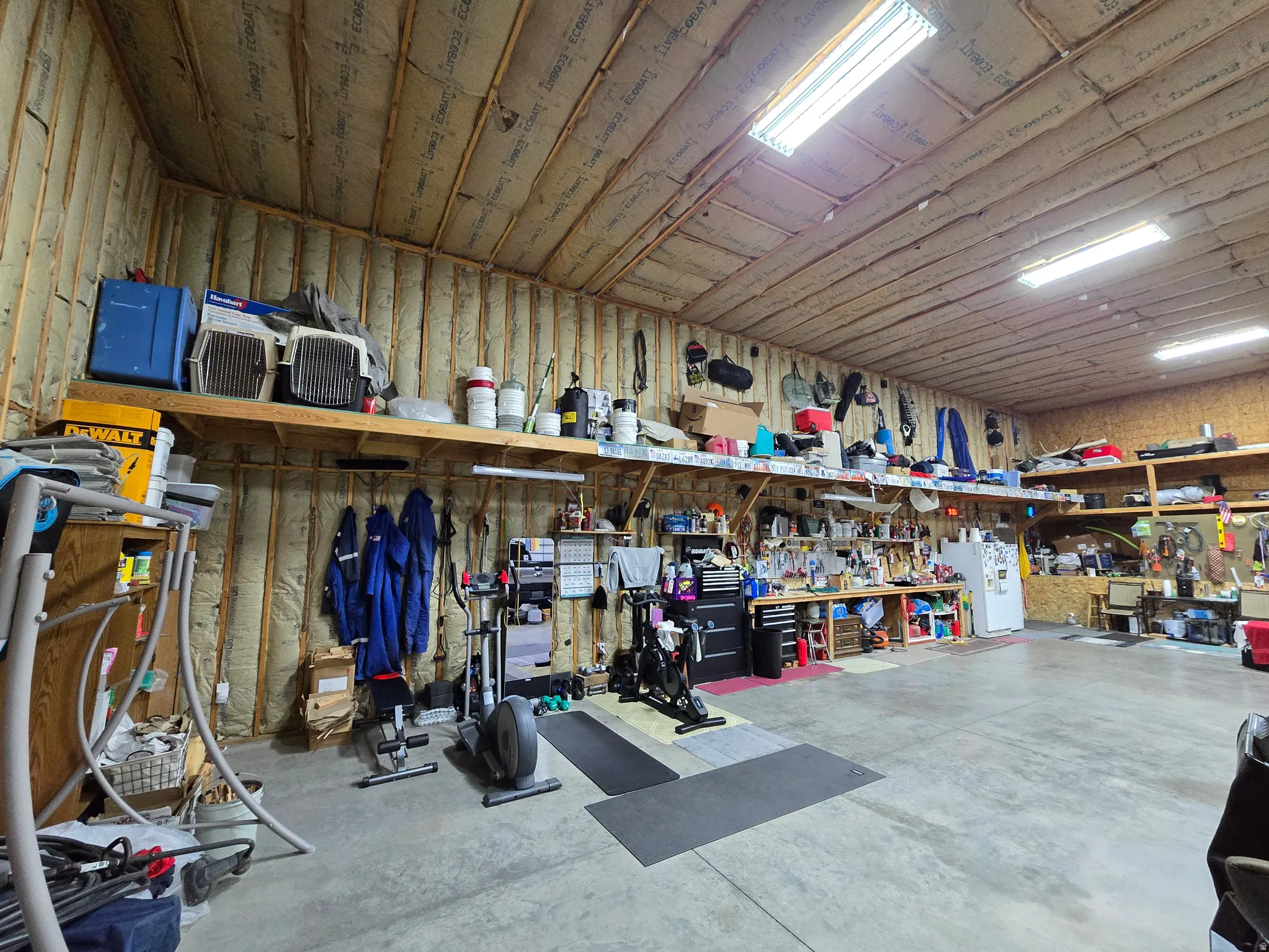 Expansive utility space featuring a concrete floor, exposed wood ceiling beams, and integrated fluorescent lighting
