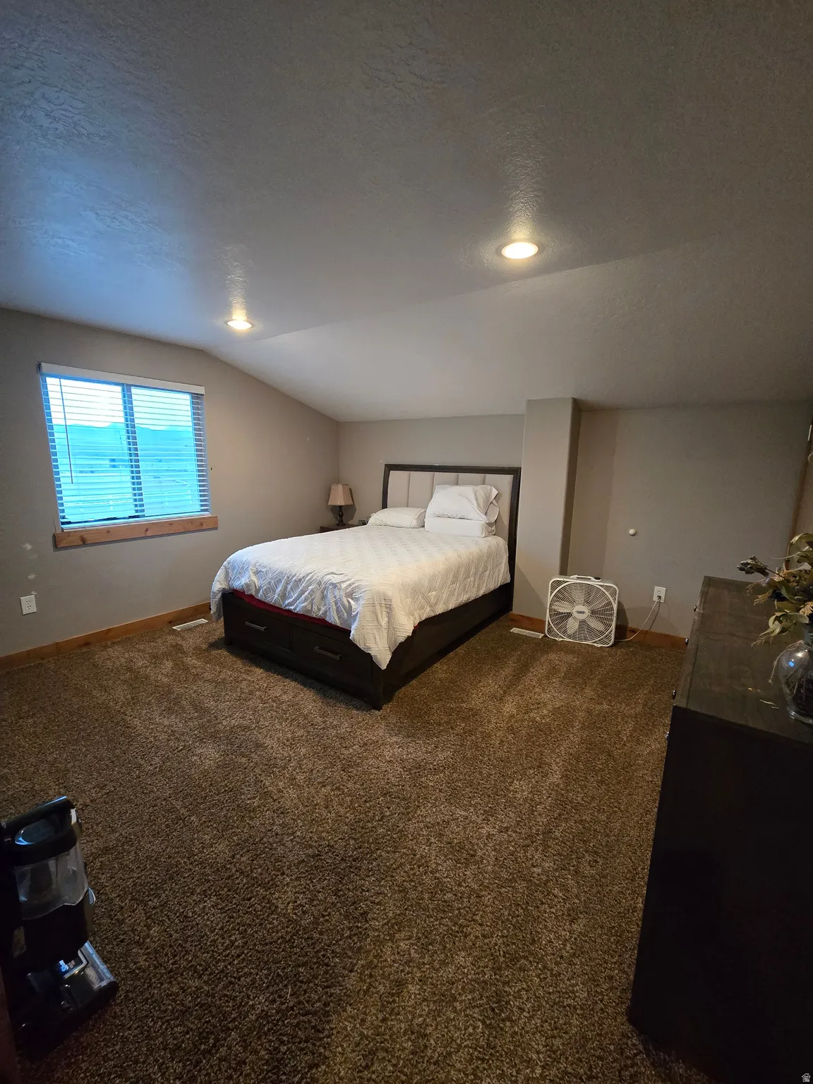 Spacious room featuring vaulted ceilings with recessed lighting, a large window with blinds, and brown carpet flooring
