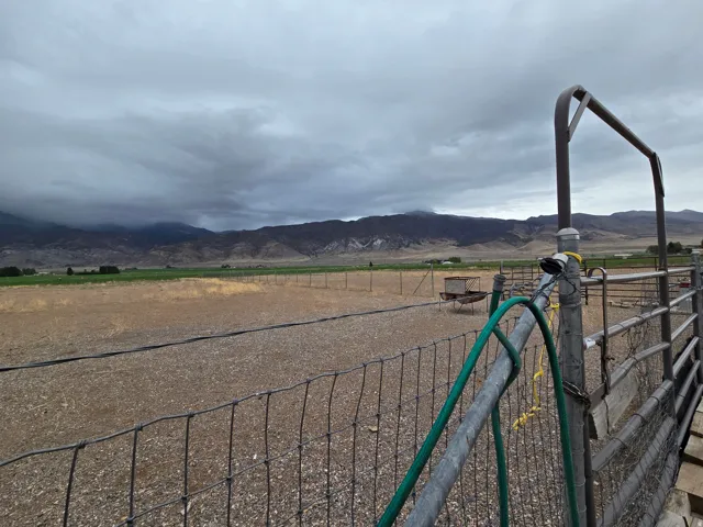 Expansive land parcel featuring fencing, an additional fenced enclosure, and distant mountain topography