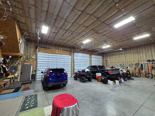 Spacious garage featuring a concrete floor, two large overhead doors, exposed wood framing, and fluorescent lighting