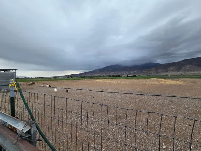 Expansive agricultural land featuring a wire fence, distant mountain range, and a covered structure