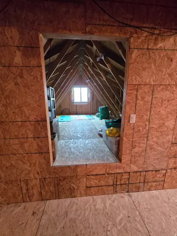 Attic space featuring exposed wood framing, a single window, and unfinished oriented strand board walls and flooring
