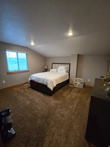 Spacious room featuring vaulted ceilings with recessed lighting, a large window with blinds, and brown carpet flooring