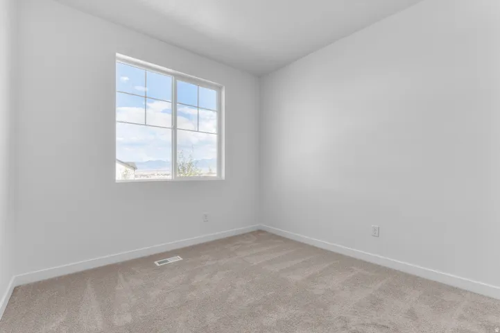 Spacious room featuring a large window with grid panes, textured white walls, neutral carpeting, and white baseboards