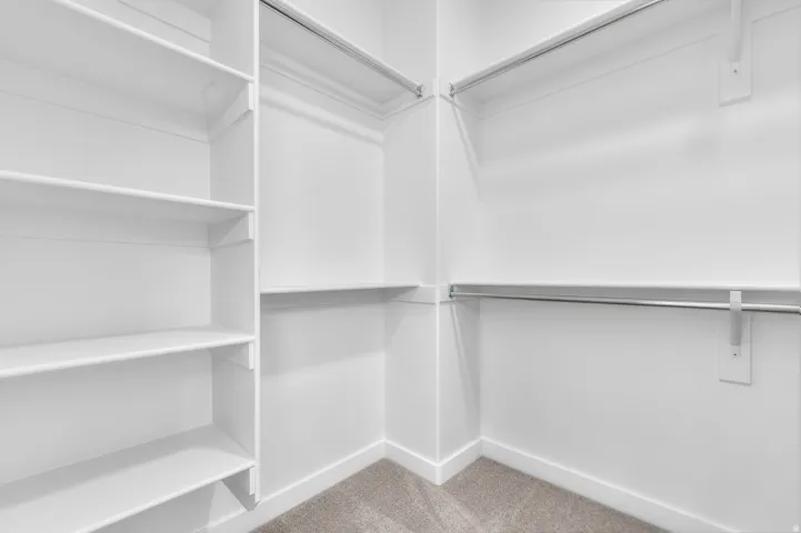 Walk-in closet featuring white built-in shelving, multiple hanging rods, white baseboards, and light-toned carpeting