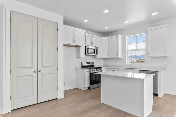 Contemporary kitchen featuring white cabinetry, a central island, stainless steel appliances, light countertops, and wood-finish flooring