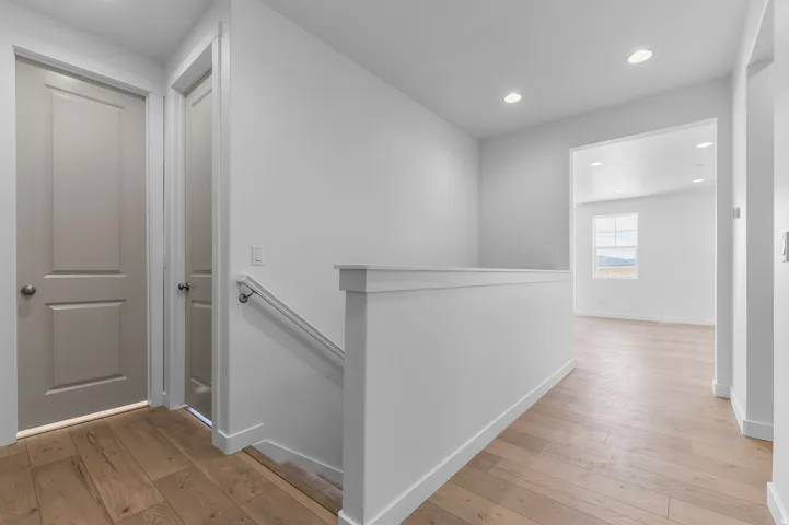Upper-level landing featuring light wood-finish flooring, recessed lighting, white trim work, and a painted handrail