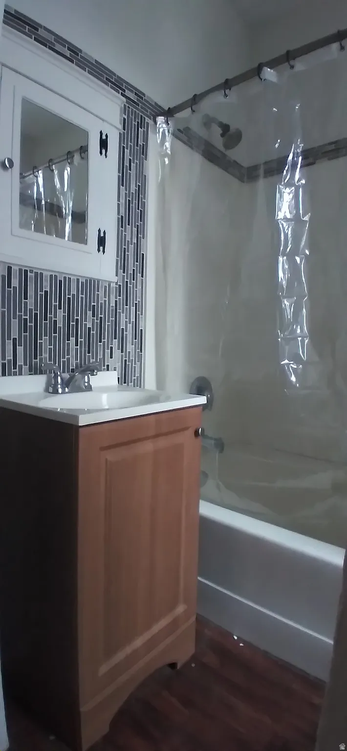Bathroom featuring wood-finish flooring, a vanity with a white countertop and integrated sink, chrome faucet, a white medicine cabinet, and a tiled shower surround