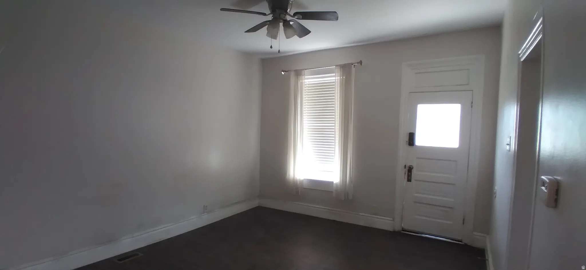 Room featuring dark wood-finish flooring, a ceiling fan, and a window with blinds