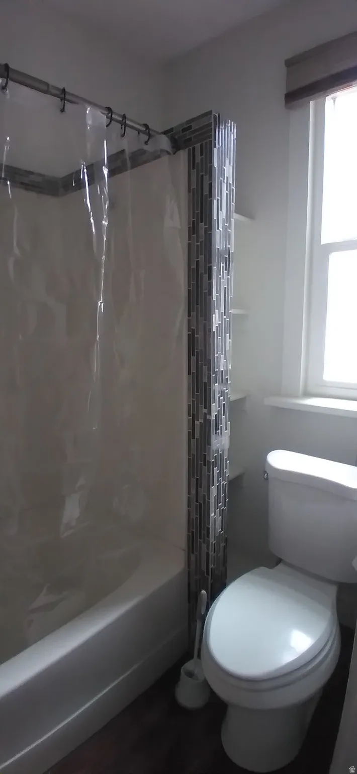 Bathroom featuring a tub/shower combination, decorative tile accent, white toilet, and wood-finish flooring