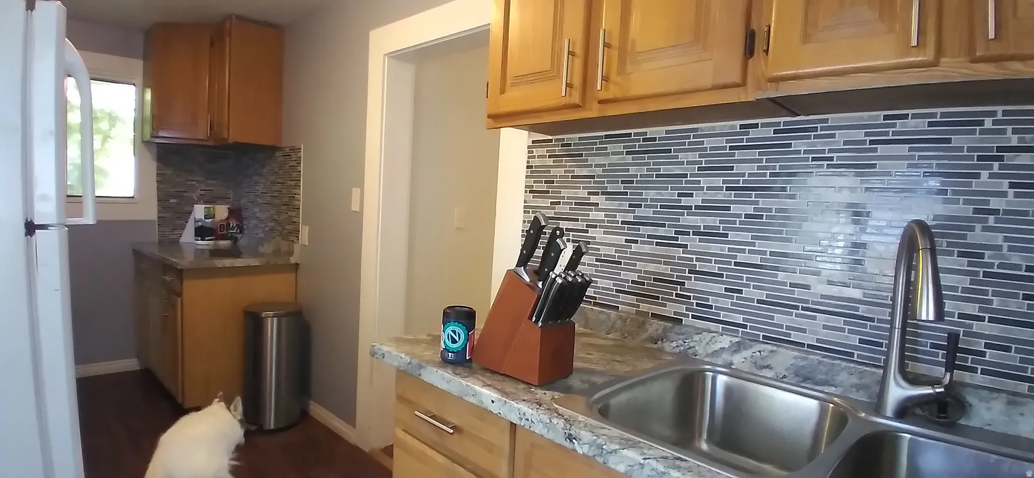 Kitchen featuring wood-finish cabinetry, a mosaic tile backsplash, and a double basin stainless steel sink with a high-arch faucet