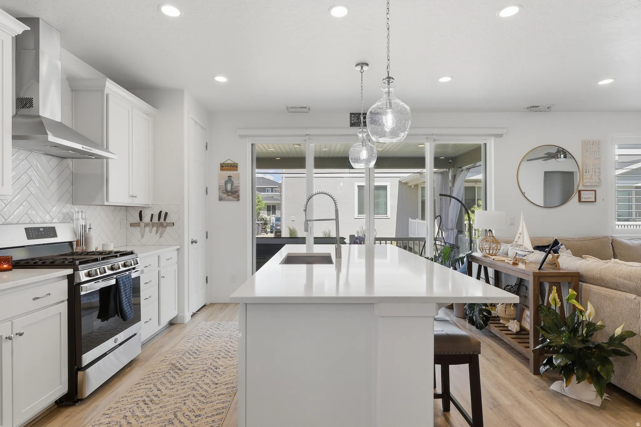 Contemporary kitchen featuring a white island with an undermount sink, pendant lighting, stainless steel appliances, and a herringbone tile backsplash