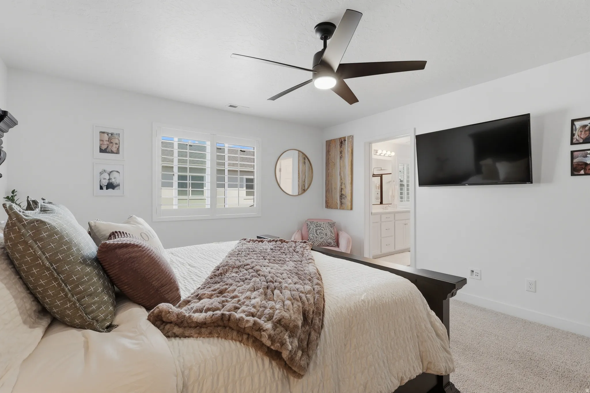 Bright bedroom featuring a large window with plantation shutters, a ceiling fan with integrated lighting, and carpeted flooring