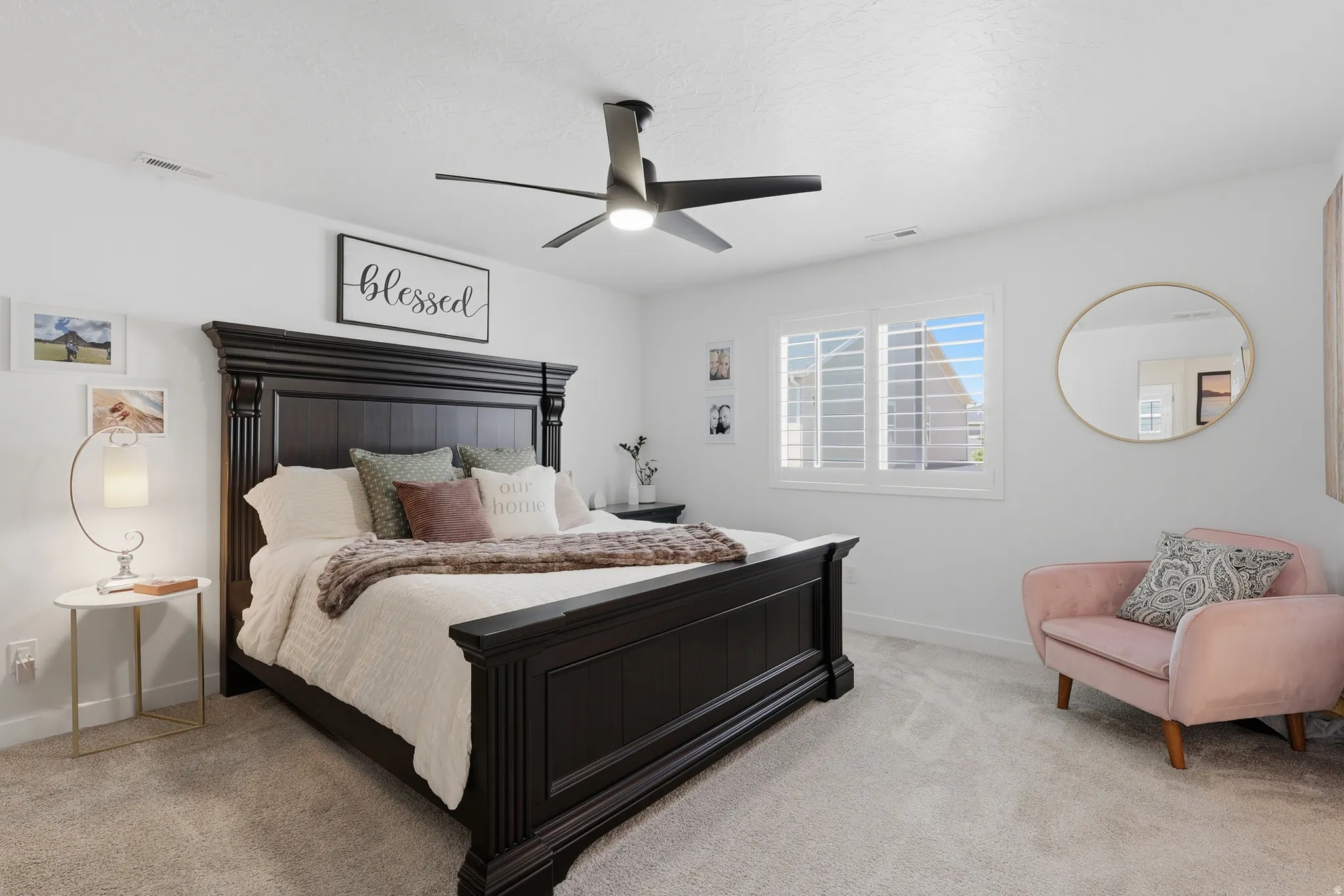 Spacious bedroom featuring light-colored carpeting, a large window with plantation shutters, a modern ceiling fan, and ample wall space