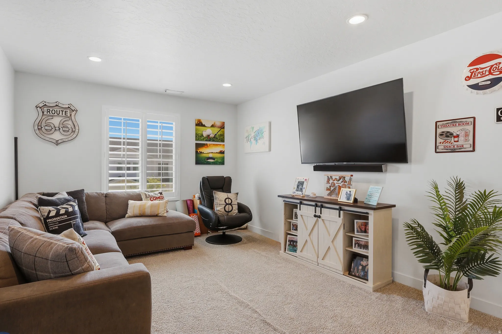Carpeted entertainment area featuring a wall-mounted display, recessed lighting, and a window with plantation shutters