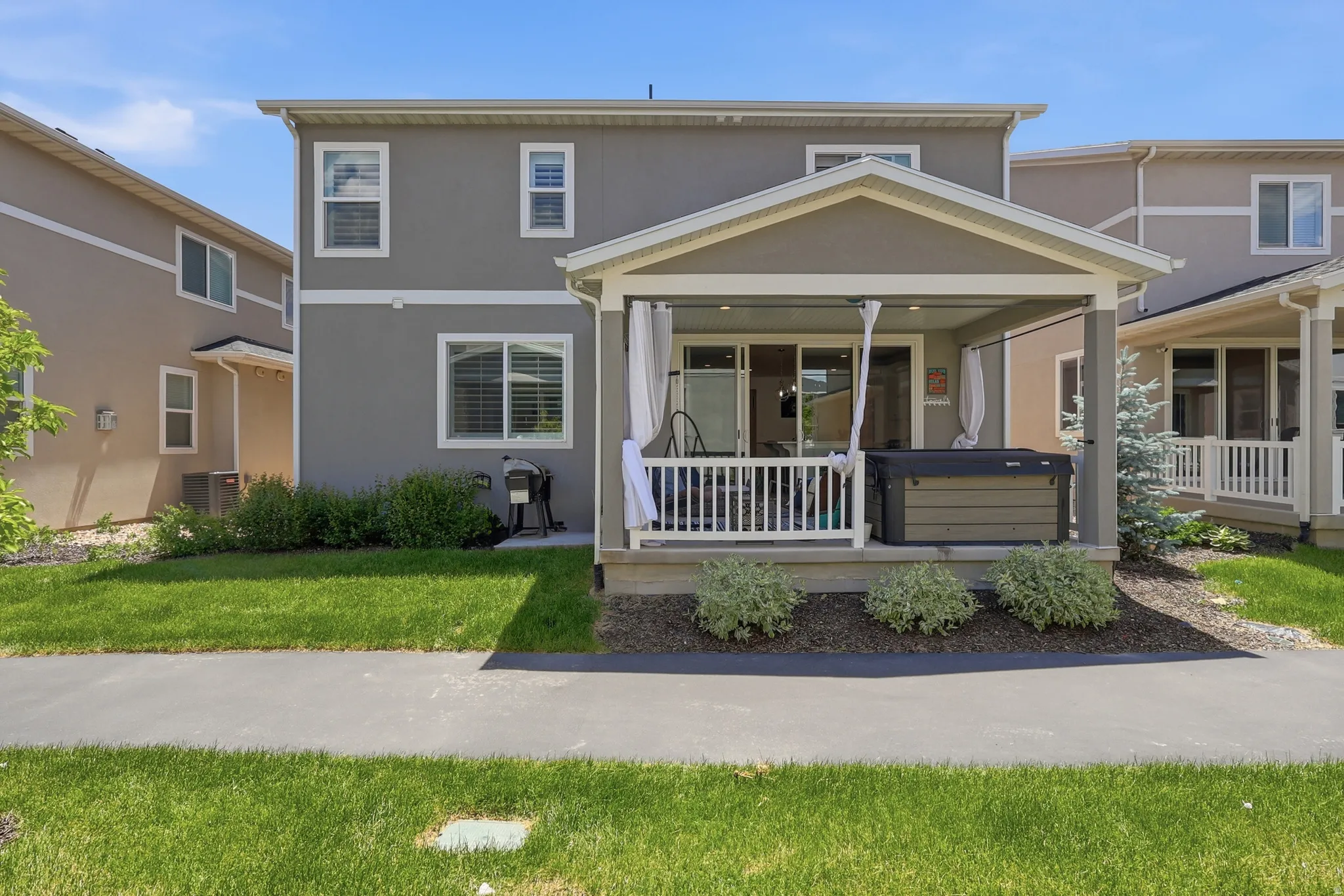 Rear exterior featuring a covered patio with white railing, sliding glass doors, and a built-in spa
