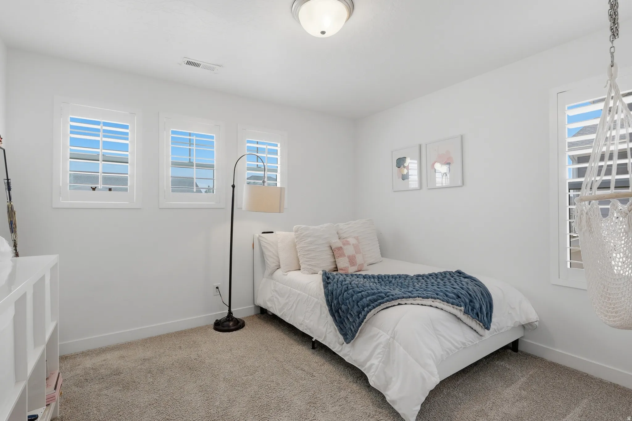 Neutral-toned room featuring a single window with plantation shutters, two additional windows, and a flush-mount ceiling light