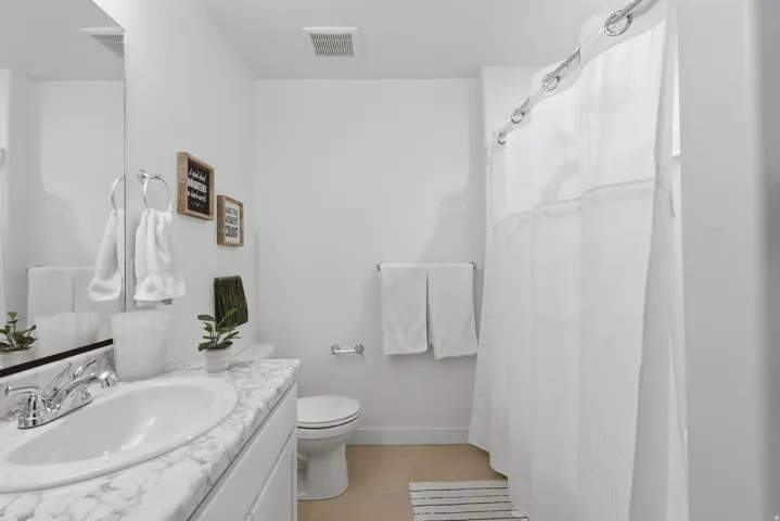 Bathroom featuring a white vanity with a marble-look countertop, an undermount sink with chrome fixtures, a toilet, and a shower with a white shower curtain