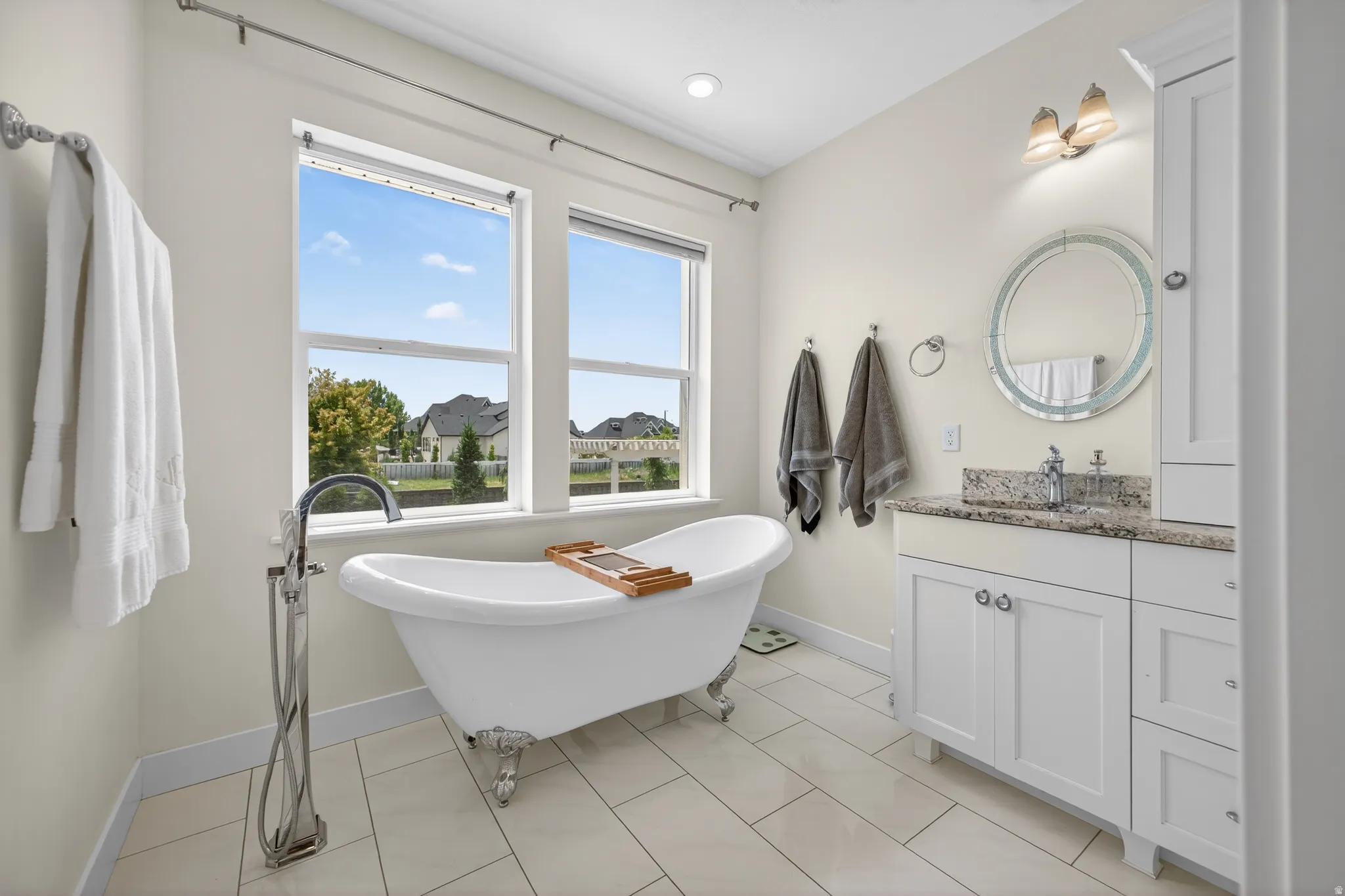 Freestanding clawfoot tub with a floor-mounted faucet, dual windows, and light-toned plank flooring