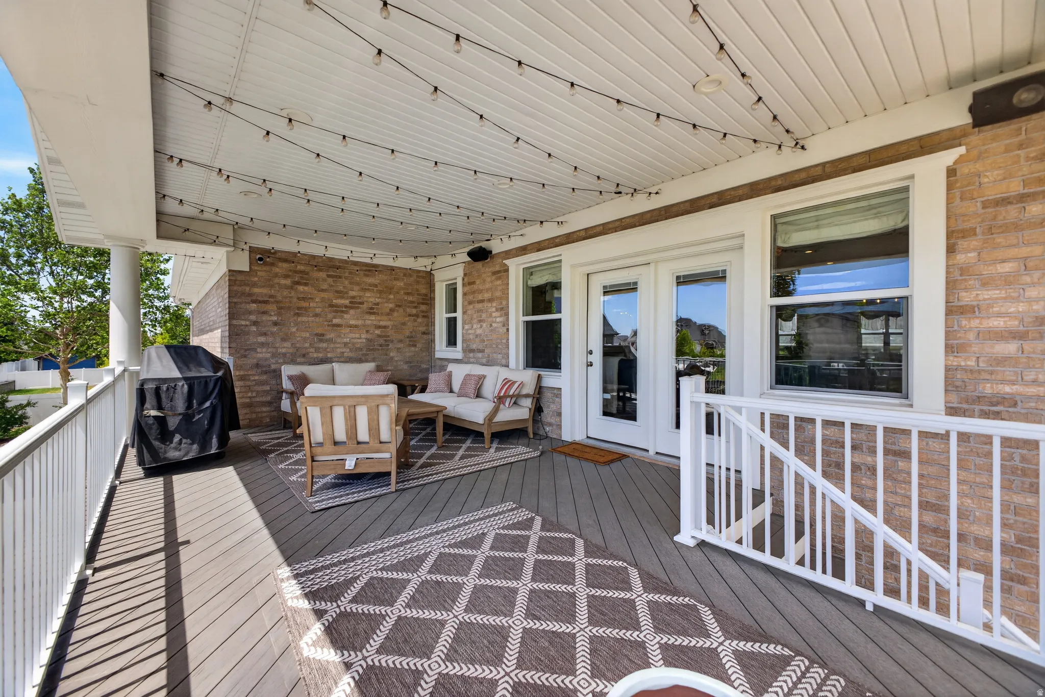 Expansive covered deck featuring composite decking, white railing, and a brick exterior