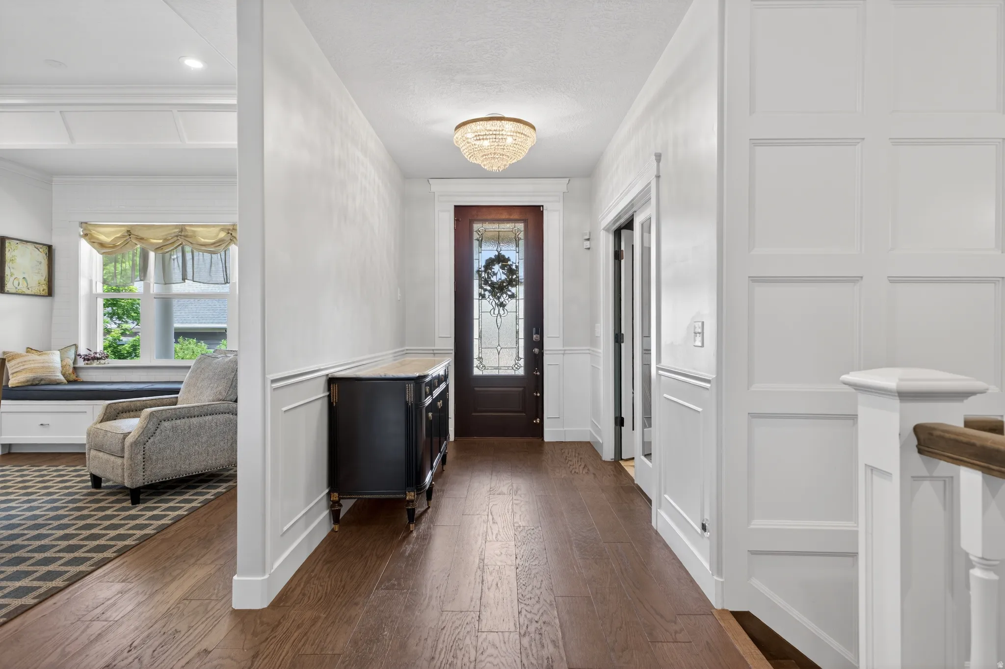 Hardwood flooring extending through the entry, detailed wainscoting, and a decorative crystal chandelier