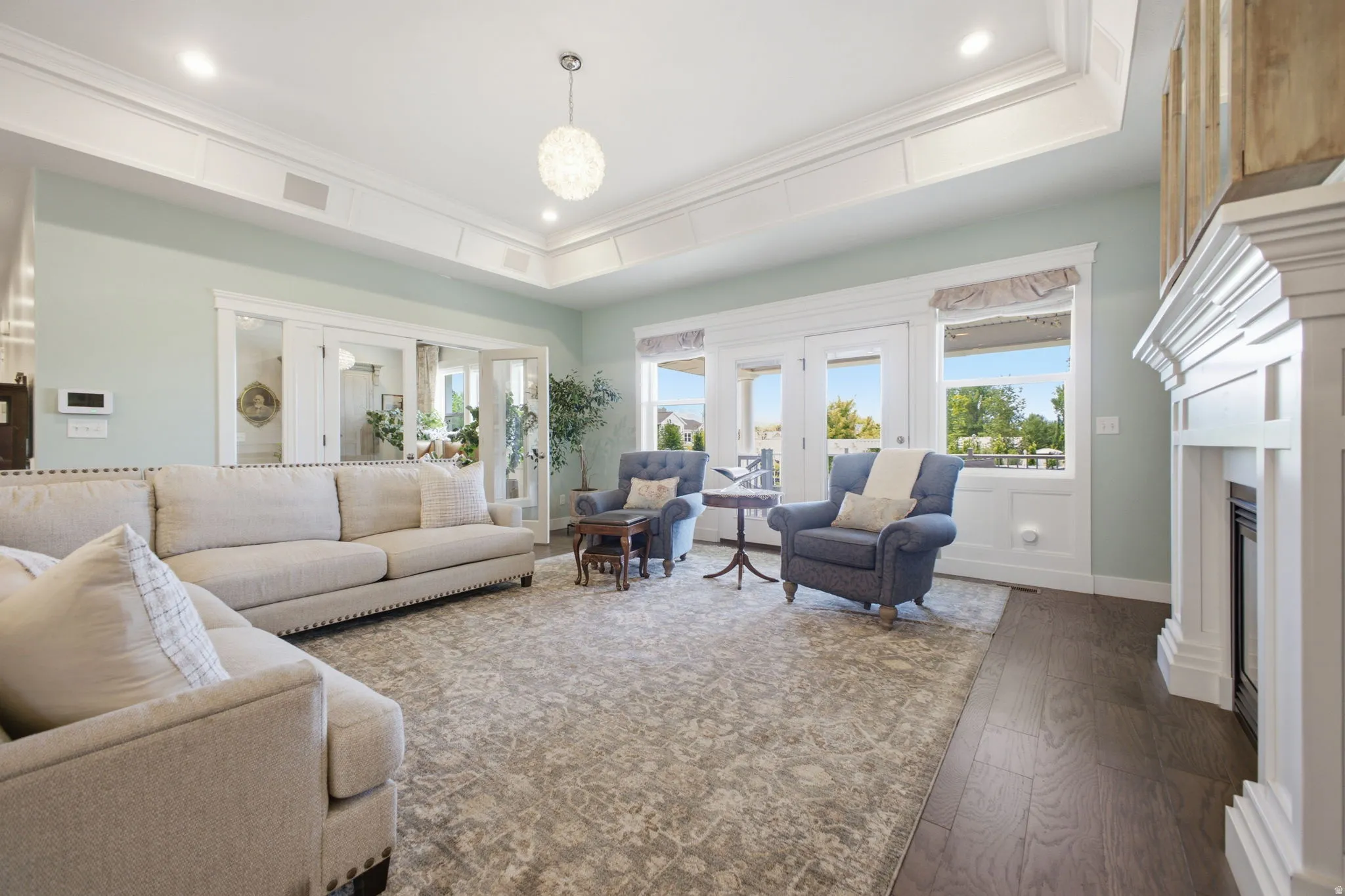 Spacious living area featuring coffered ceilings with recessed lighting, a decorative chandelier, a white mantel fireplace, and dark wood-finish flooring