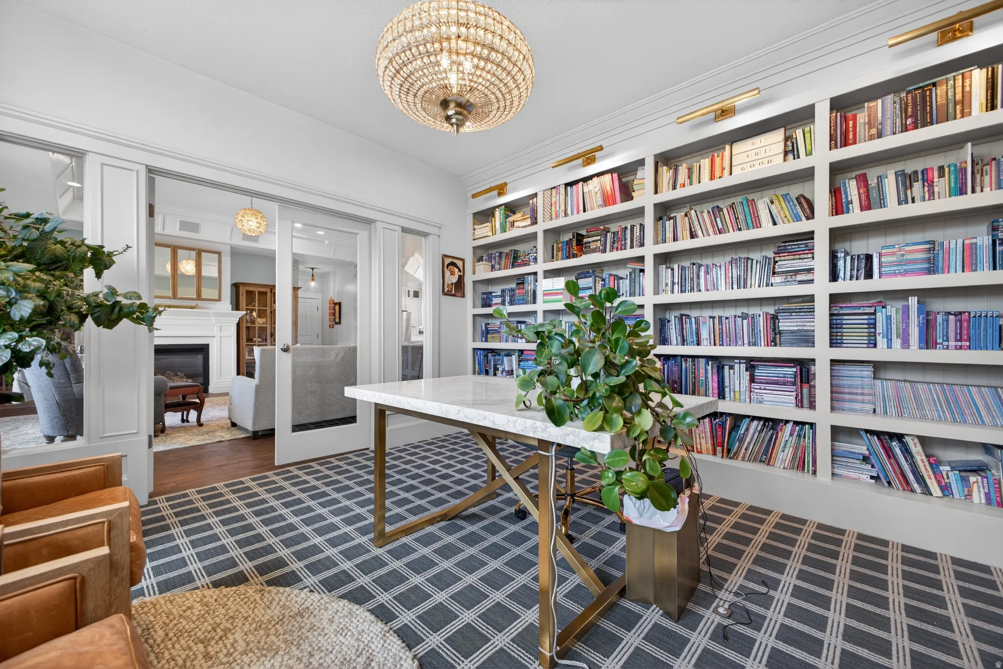 Custom built-in shelving with integrated lighting, glass pocket doors, and a decorative chandelier