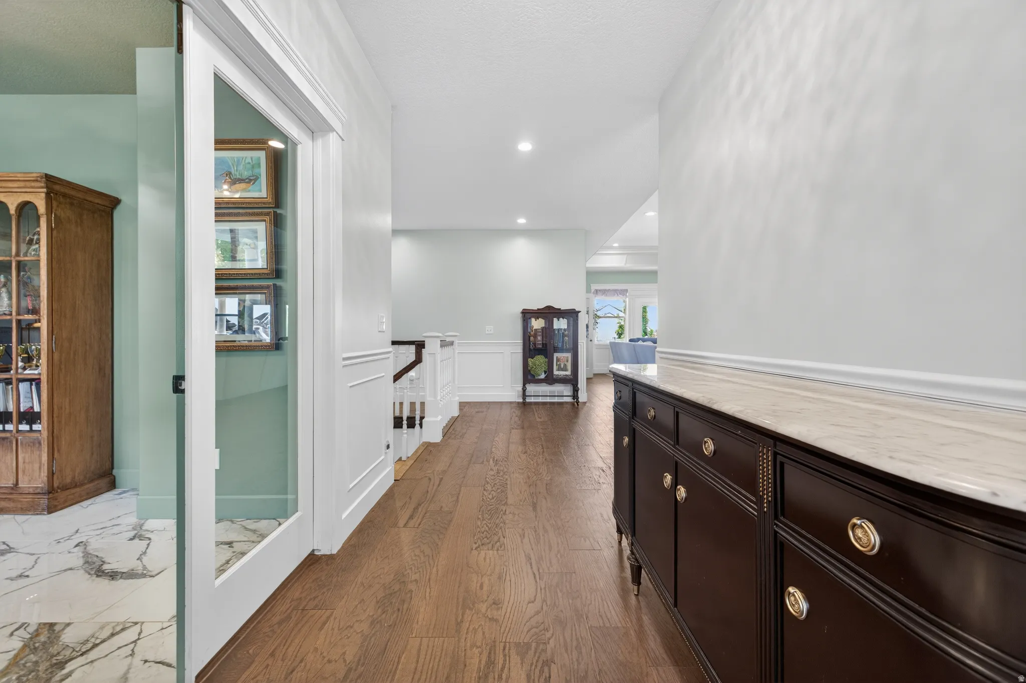 Expansive hallway featuring wood-finish flooring, white wainscoting, and recessed lighting