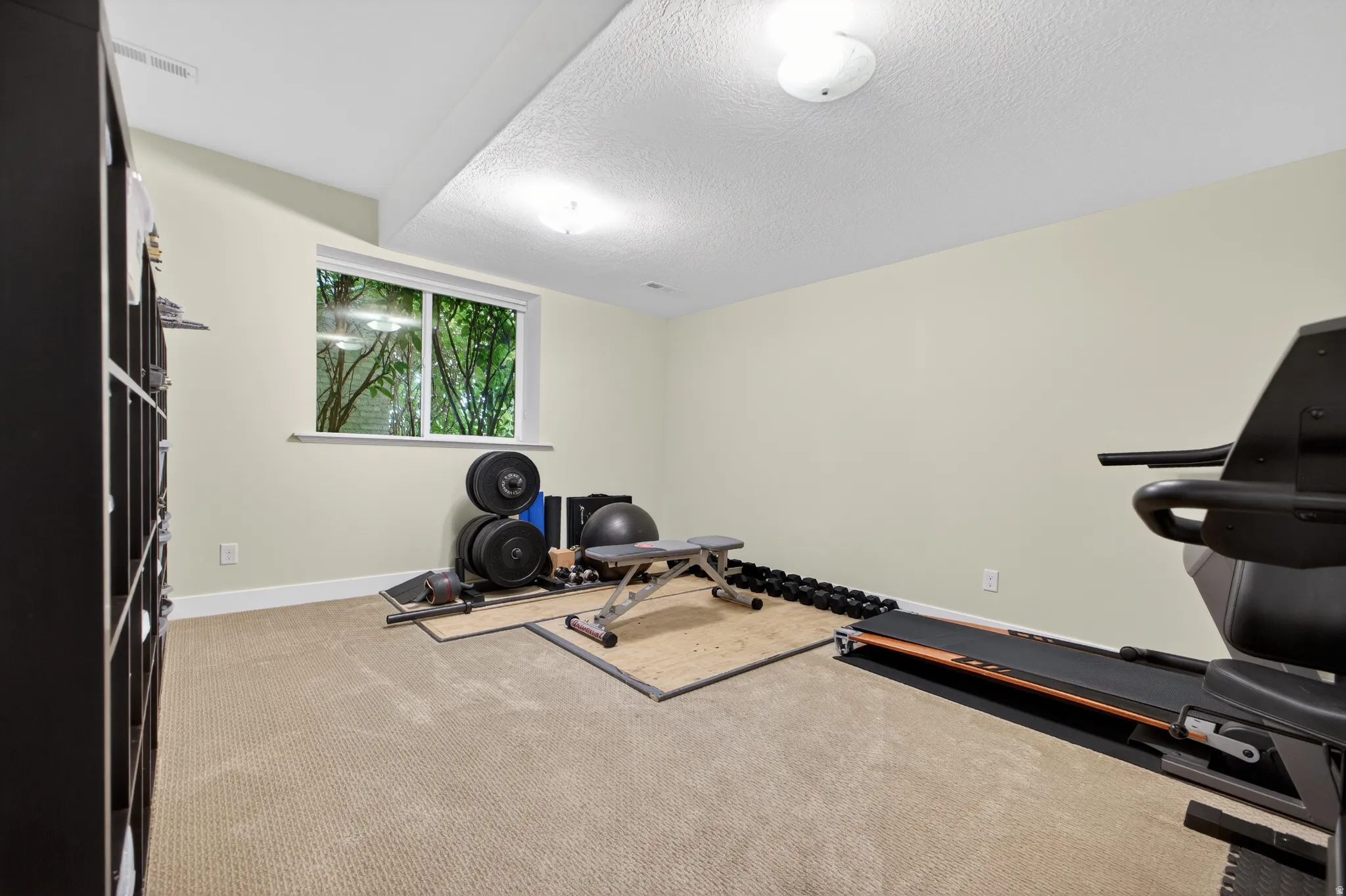 Carpeted room featuring a white-trimmed window, light-colored walls, recessed ceiling lighting, and a built-in shelving unit