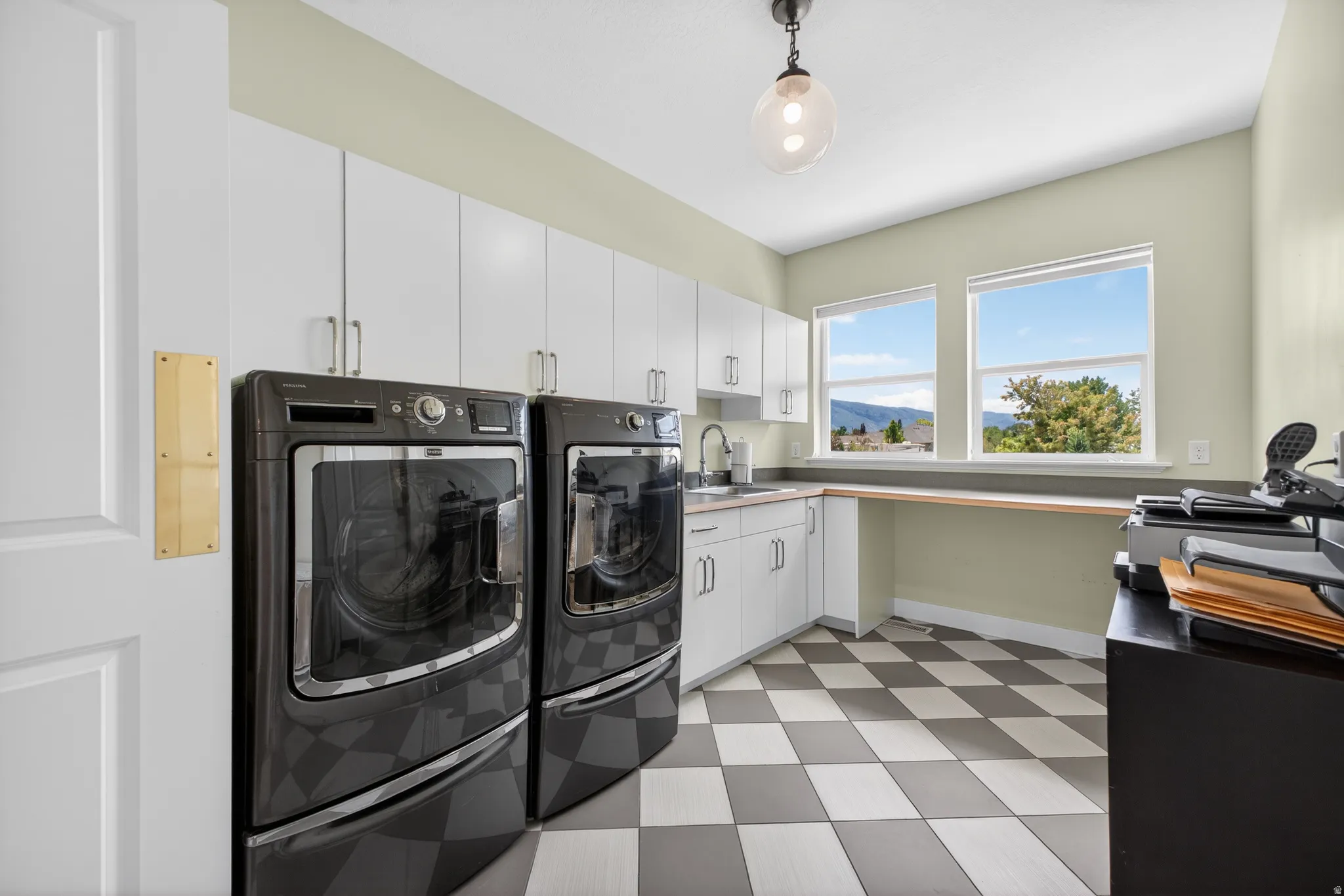 Utility room featuring checkerboard flooring, extensive white cabinetry, and two windows offering a distant mountain landscape