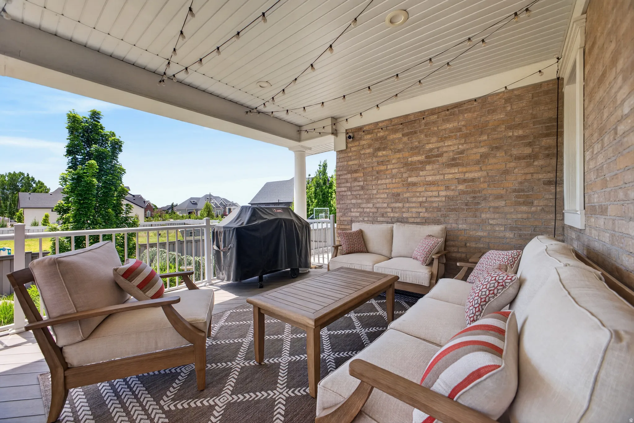 Expansive covered patio featuring a brick exterior wall, white railing, outdoor ceiling fan, and string lights
