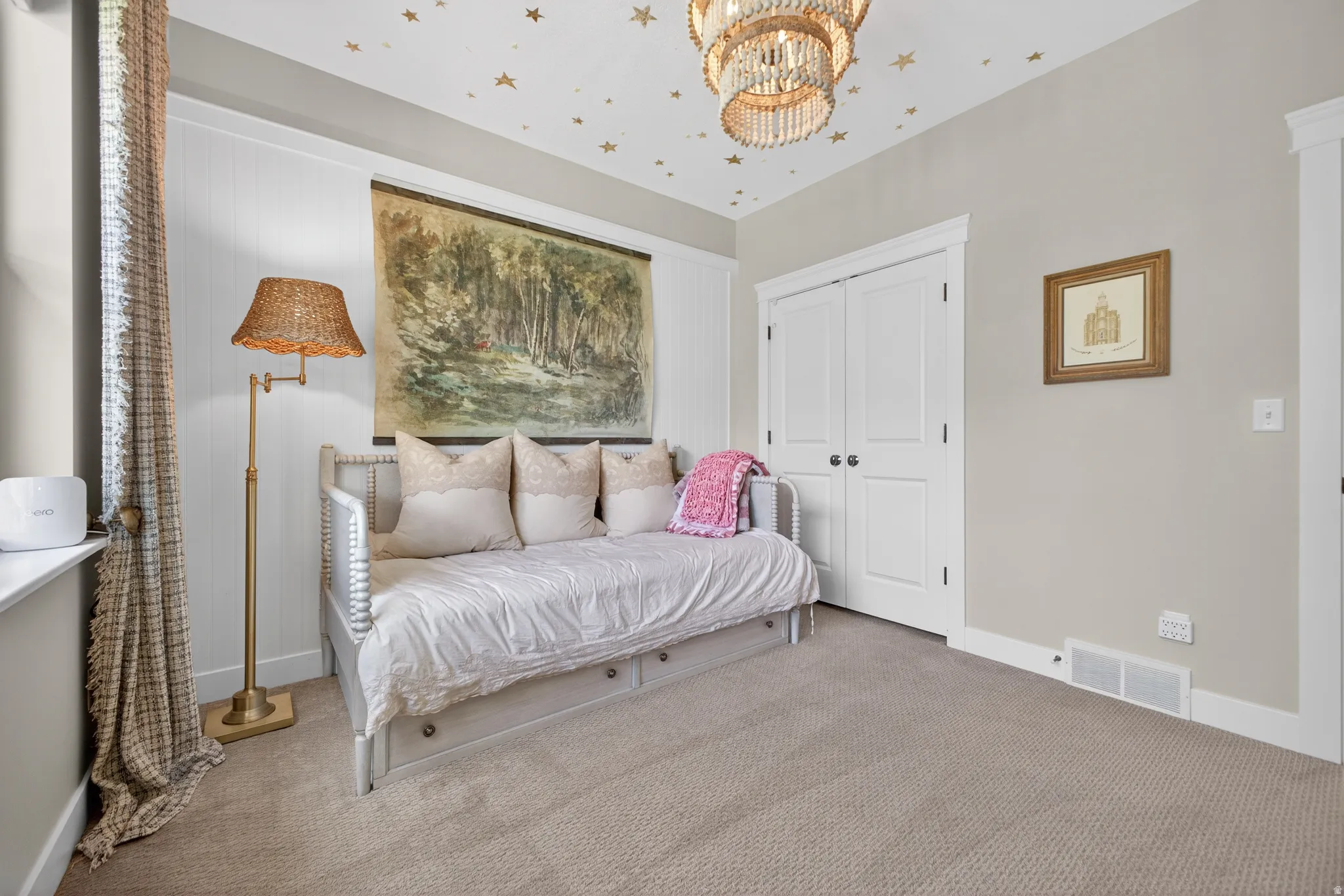 Carpeted room featuring a double-door closet with black hardware, a window with patterned curtains, and a decorative ceiling fixture