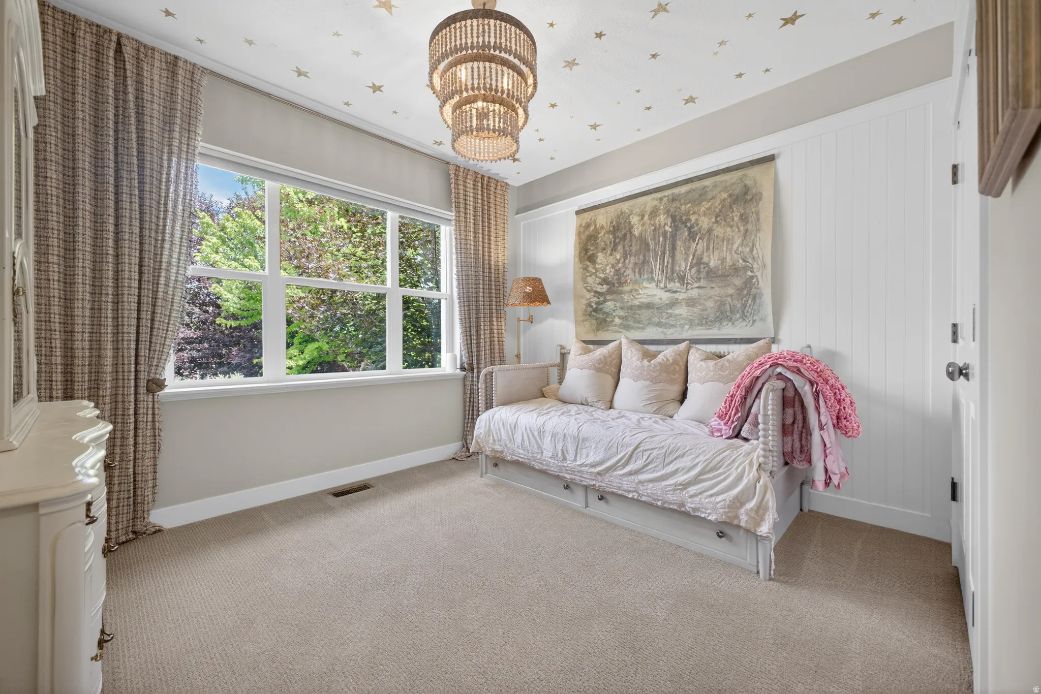 Bright room featuring a large multi-pane window, neutral-toned carpeting, white wainscoting, and a tiered chandelier