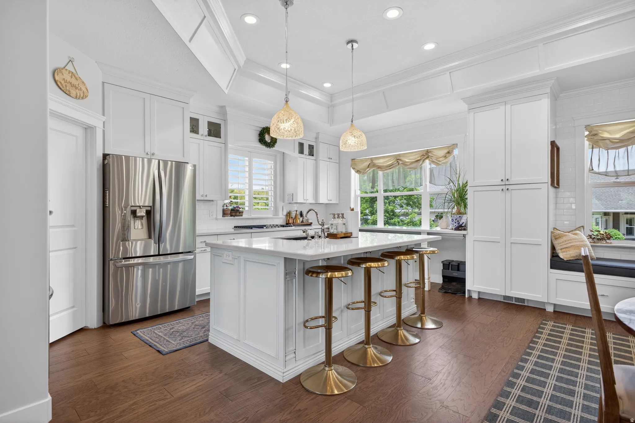 White kitchen featuring a central island with seating, stainless steel appliances, wood-finish flooring, white cabinetry, and a window seat with built-in storage
