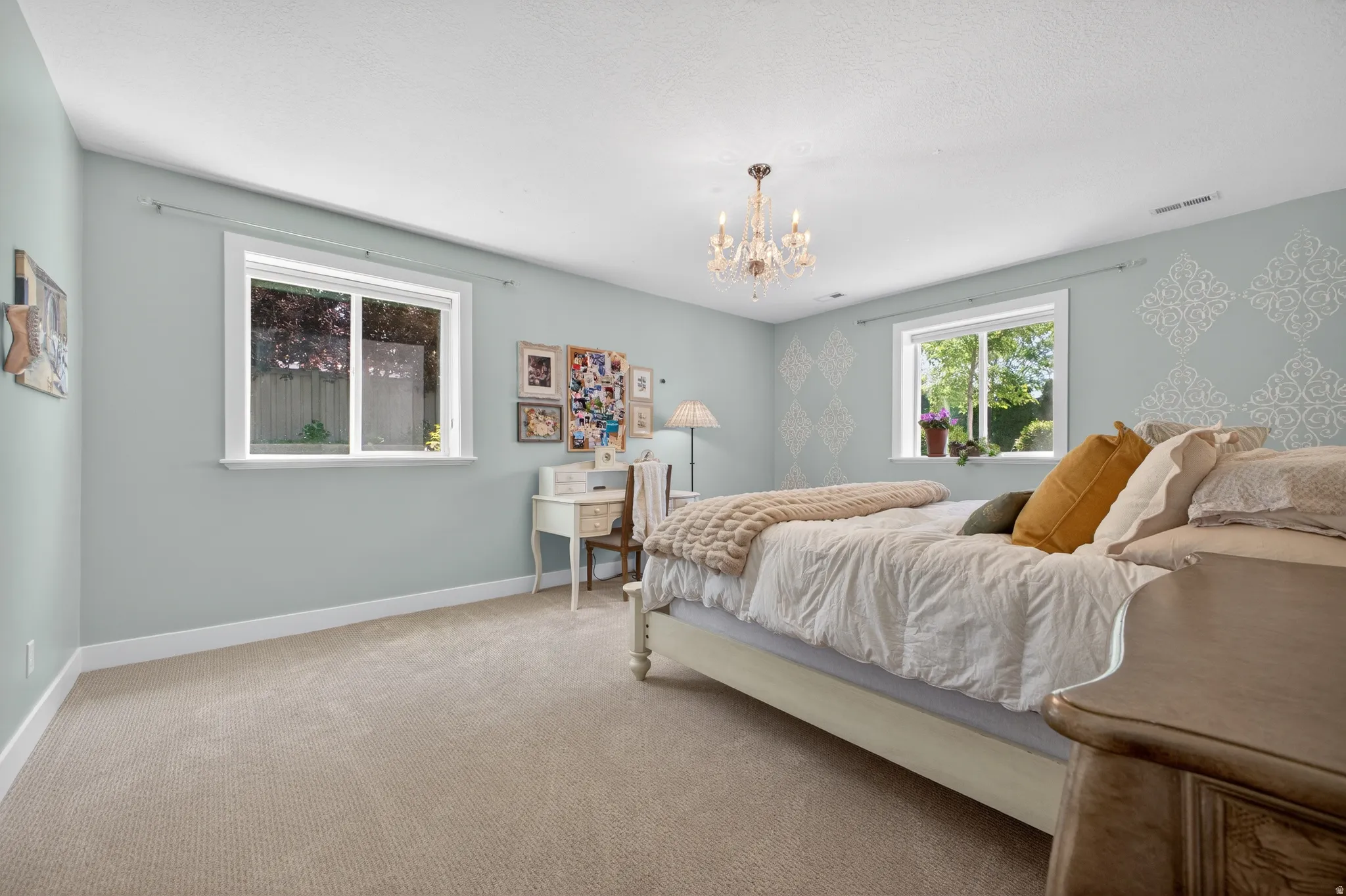 Room featuring neutral-toned carpeting, light blue walls with decorative stenciling, white trim, and two windows