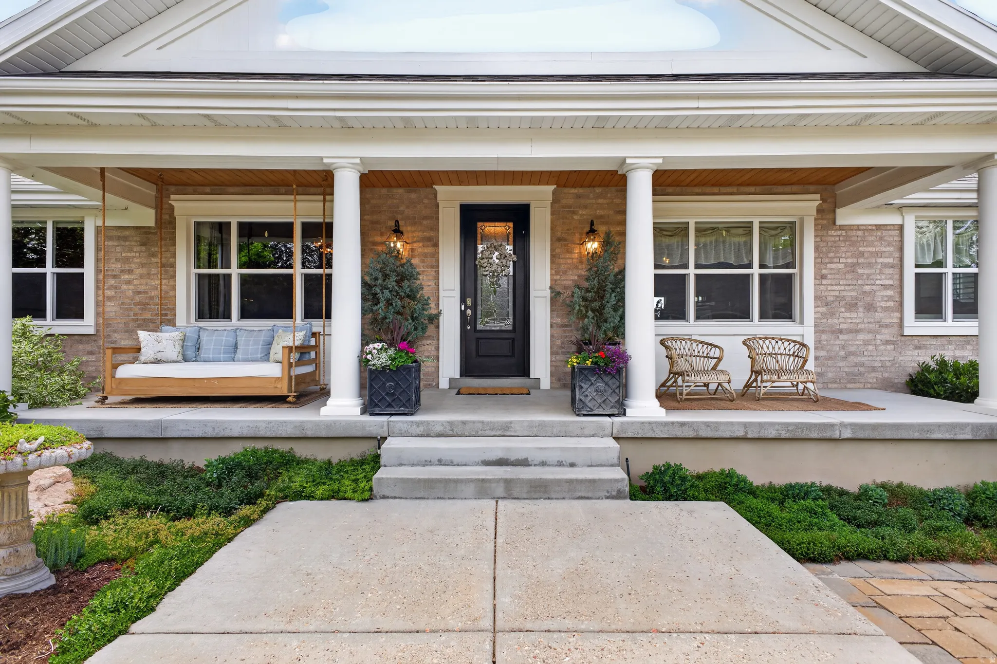 Brick exterior with a covered front porch featuring white columns and a central black entry door with decorative glass