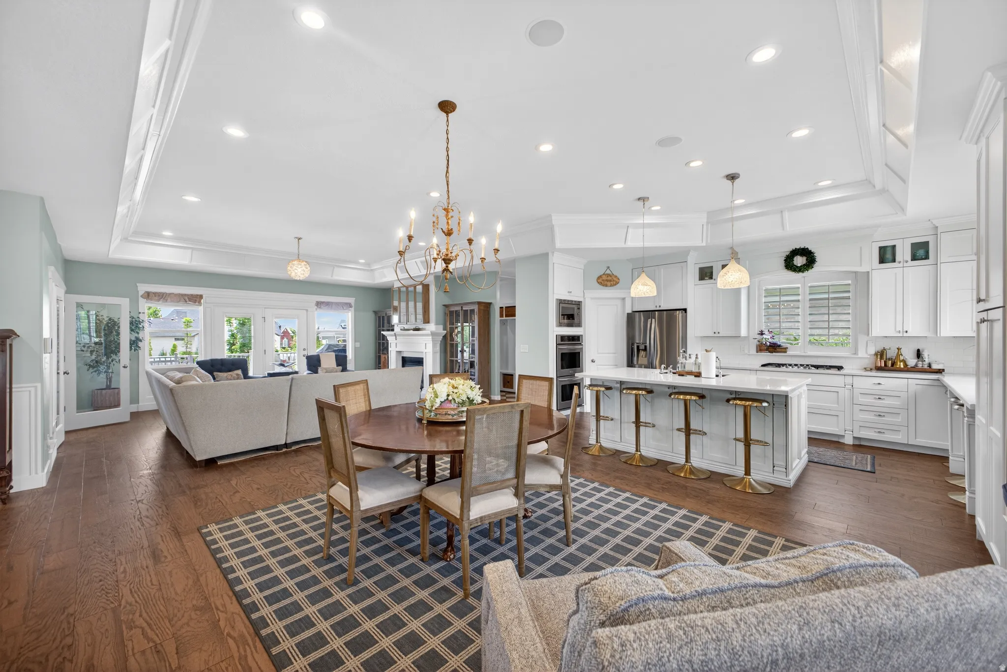 Open-concept living space featuring wood-finish flooring, a tray ceiling with recessed lighting, and a white kitchen with a large island