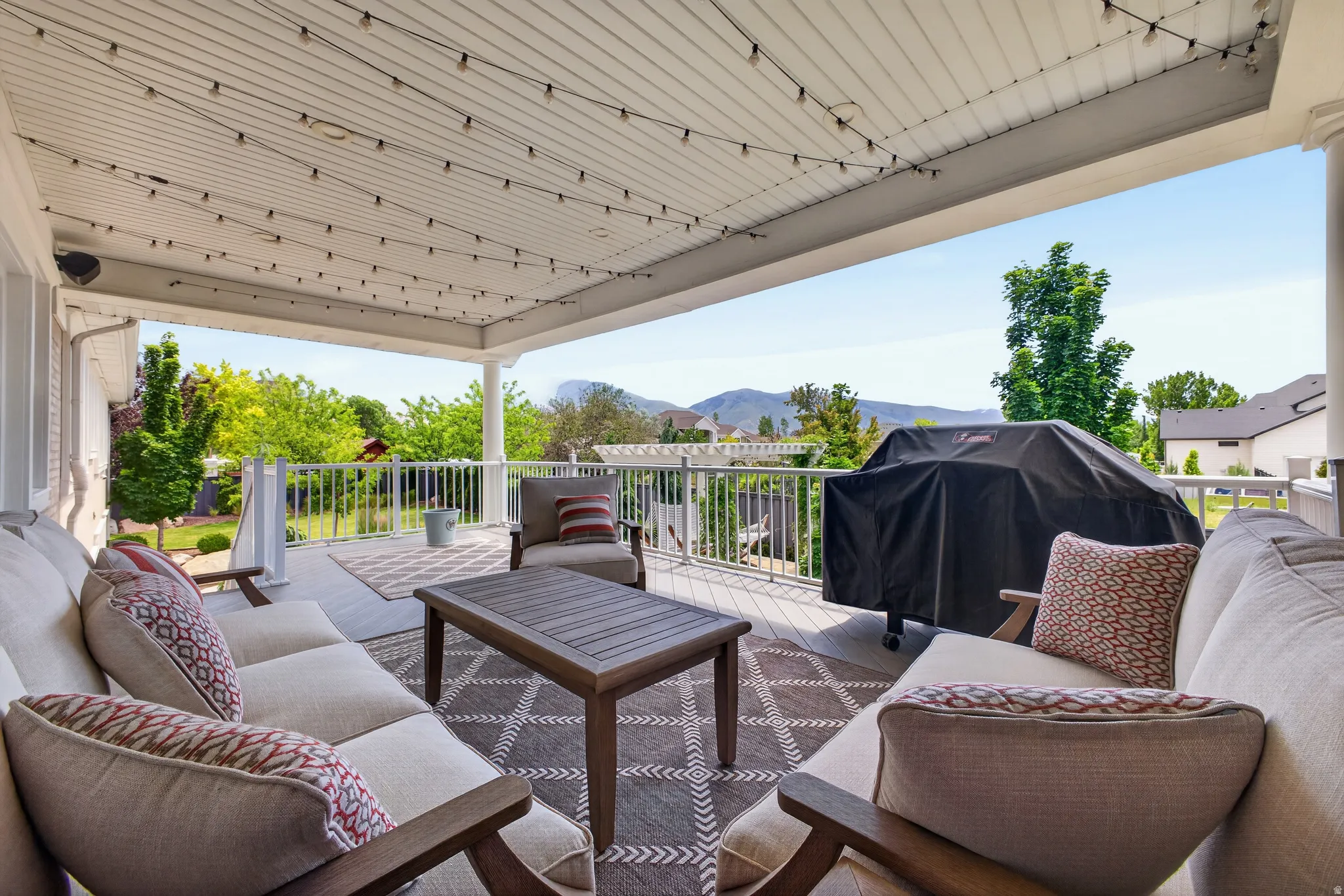 Spacious covered deck featuring a white railing, a patterned outdoor rug, and string lighting