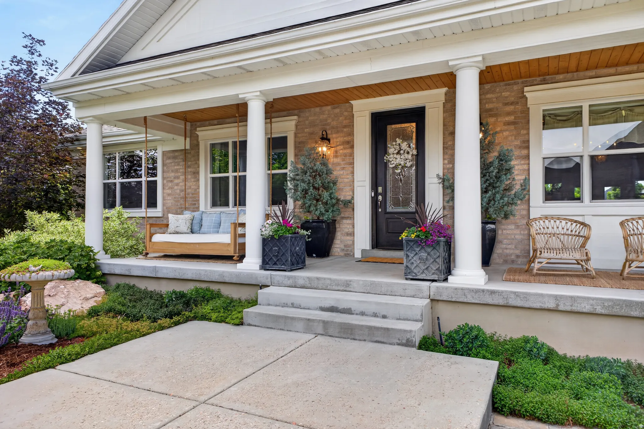 Brick exterior featuring a covered porch with white columns, concrete steps, a wood-paneled ceiling, and a dark-paneled door with decorative glass