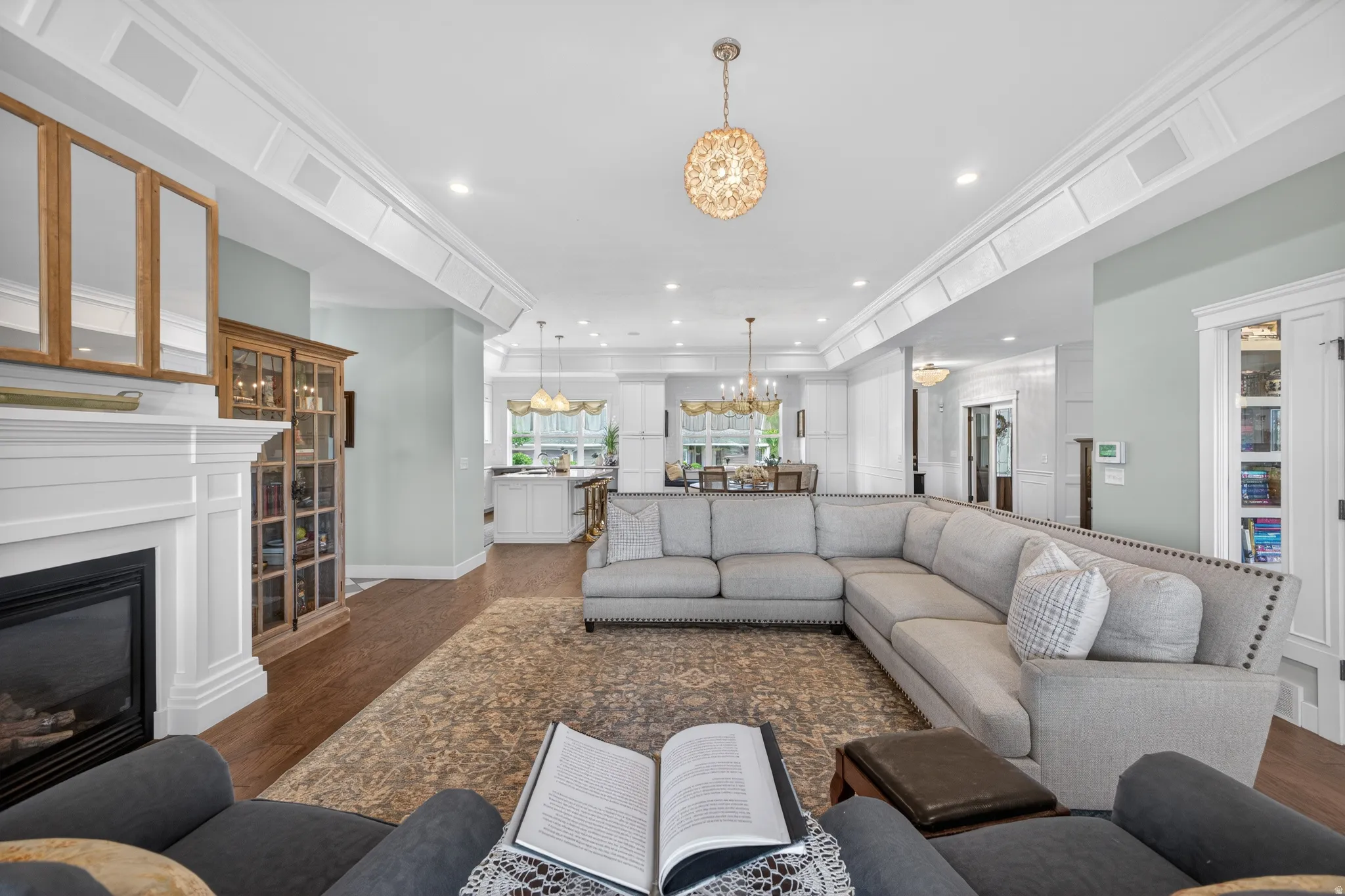 Spacious living area featuring rich wood-finish flooring, an ornate area rug, and a white mantel fireplace with a dark hearth