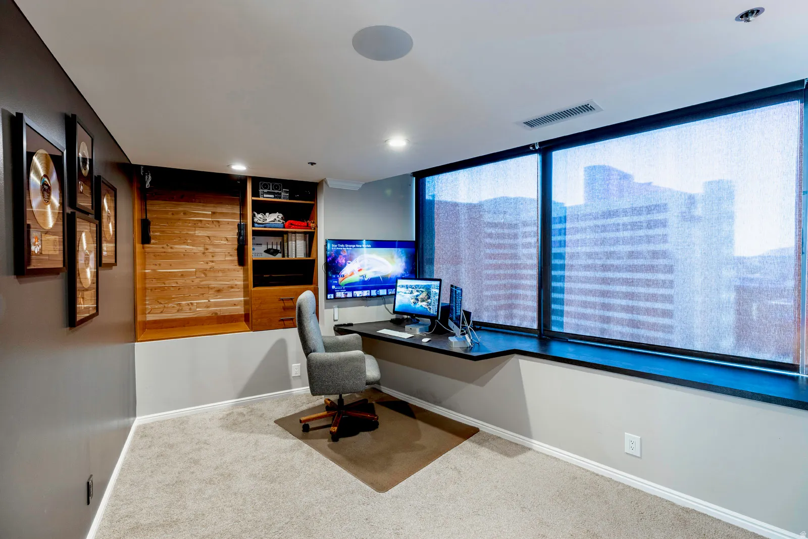 Dedicated workspace featuring a built-in desk, expansive windows with roller shades, recessed lighting, and a built-in storage unit with a wood-finish barn door
